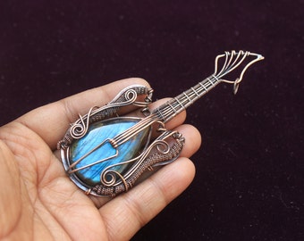 May include: A copper wire wrapped guitar pendant with a blue labradorite gemstone. The pendant is in the shape of a guitar with intricate wire details.