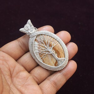 May include: Silver wire wrapped pendant featuring a brown and white tree of life stone. The pendant is oval shaped and has a silver bail.