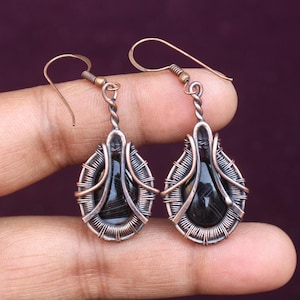 May include: A pair of dangle earrings with black agate stones wrapped in copper wire. The earrings have a teardrop shape and are suspended from a simple hook.