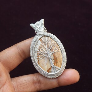 May include: Silver wire wrapped pendant featuring a brown and white tree of life stone.