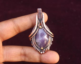 May include: A copper wire wrapped pendant featuring a purple amethyst gemstone. The pendant has a gold accent at the top and bottom.