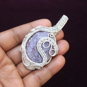 May include: A silver wire wrapped pendant featuring a purple and white gemstone. The pendant is shaped like a teardrop and has a delicate wire design.