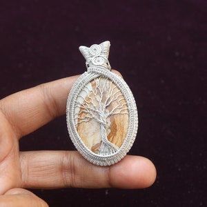 May include: A silver wire wrapped pendant featuring a tree of life design with a brown and white agate stone.