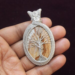May include: Silver wire wrapped pendant featuring a tree of life design with a brown and white agate stone.