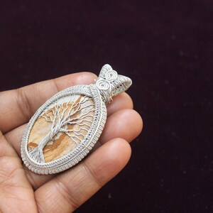 May include: A silver wire wrapped pendant featuring a tree of life design on a brown and white agate stone.