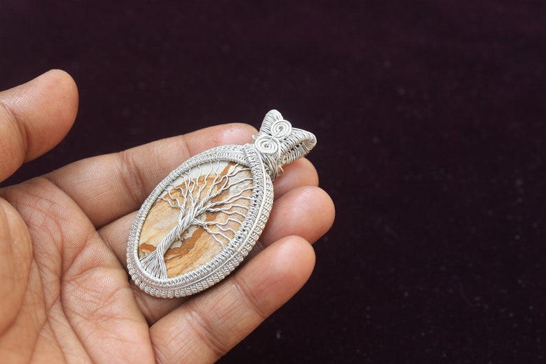 May include: A silver wire wrapped pendant featuring a tree of life design on a brown and white agate stone.