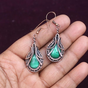 Pode incluir: Um par de brincos envoltos em fio de cobre com pedras de malaquita verde. Os brincos têm forma de lágrima e um design delicado de fio.