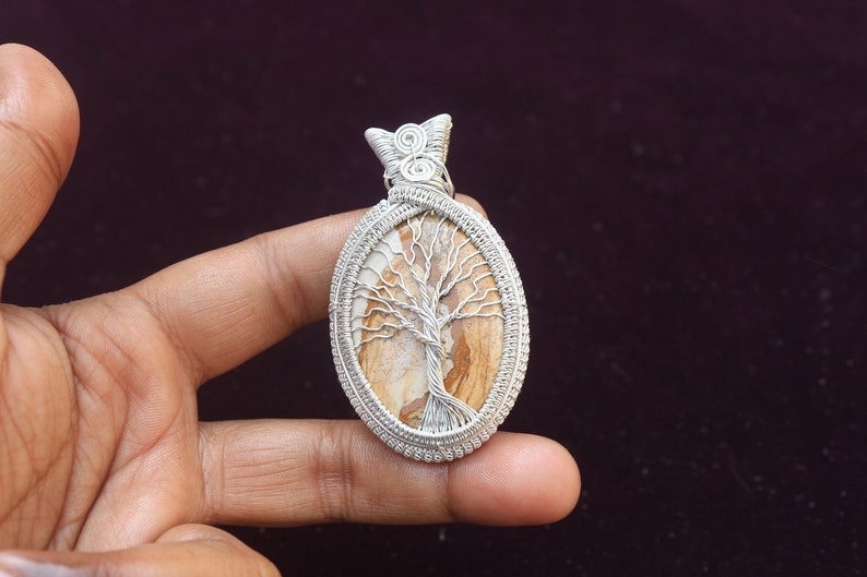 May include: A silver wire wrapped pendant featuring a tree of life design with a brown and white agate stone.