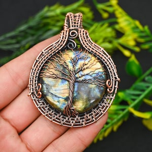 May include: A copper wire wrapped pendant featuring a round labradorite gemstone with a tree of life design. The pendant is a circular shape with a copper wire bail.