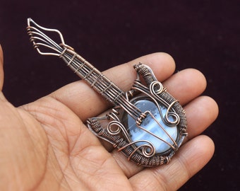 May include: A copper wire guitar pendant with a white and gray agate stone in the center. The pendant is in the shape of a guitar and has intricate wirework details.