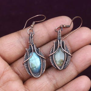 Può includere: Un paio di orecchini avvolti in filo di rame con pietre preziose di labradorite blu-verde iridescenti.