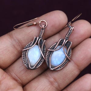May include: A pair of copper wire wrapped earrings with oval moonstone gemstones. The earrings have a delicate, handcrafted look.