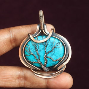 Può includere: Un ciondolo avvolto in filo di rame con una pietra turchese con un design ad albero. Il ciondolo è di forma ovale e ha un'anellina in rame.