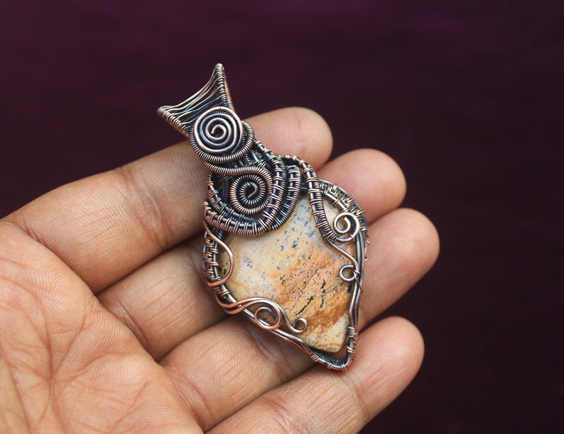 May include: A pendant featuring a brown and white agate stone wrapped in copper wire. The wire is twisted and formed into intricate designs, including spirals and loops.