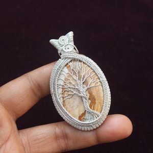 May include: Silver wire wrapped pendant featuring a brown and white tree of life stone.