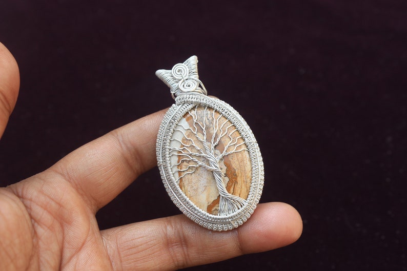 May include: Silver wire wrapped pendant featuring a brown and white tree of life stone.