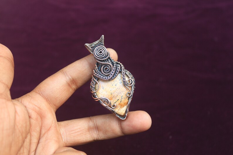 May include: A pendant featuring a light brown stone wrapped in copper wire with intricate designs. The wire is twisted and curled, creating a unique and eye-catching piece of jewelry.