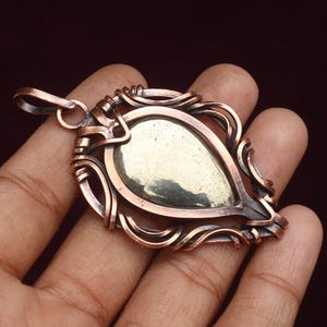 May include: A handcrafted copper pendant with a teardrop-shaped pyrite stone. The pendant features intricate wire wrapping and a loop for a chain. The copper has a warm, reddish-brown hue, and the pyrite stone has a metallic, gold-like appearance.