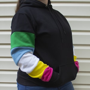 Op de afbeelding: Zwart hoodie met een kleurrijke gestreepte mouw. De mouw is gestreept in groen, blauw, wit, geel en roze.