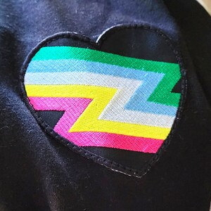 May include: A black heart-shaped patch with a colourful zigzag pattern in pink, yellow, white, light blue, and green.