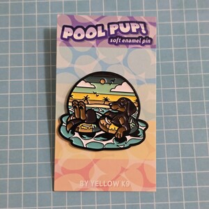 May include: A soft enamel pin featuring a dachshund dog relaxing in a pool float. The pin has a colorful design with the words "POOL PUP!" at the top. The pin is on a card with the text "BY YELLOW K9".