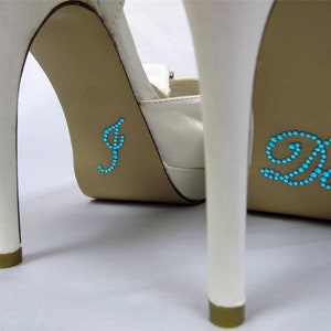 Może przedstawiać: Para białych butów na wysokim obcasie z niebieskimi zdobieniami z kryształków, które tworzą napis "I Do" na podeszwach.