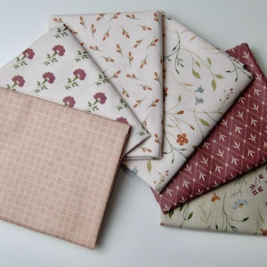 May include: A collection of six folded fabric squares featuring various patterns including a light pink grid, maroon floral prints, delicate botanical stems, and small orange and blue flowers on cream and maroon backgrounds.