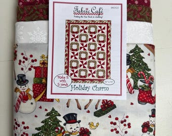 Könnte beinhalten: Ein Stapel gefalteter Stoffe mit Weihnachtsmotiven, gekrönt von einem Schnittmusterheft von Fabric Cafe mit dem Titel Holiday Charm. Das Muster zeigt ein Quilt-Design von 130 cm mal 180 cm. Die Stoffe sind mit Schneemännern, Rehen und Bäumen bedruckt.