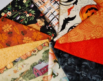 Könnte beinhalten: Eine Sammlung gefalteter Stoffquadrate mit Herbst- und Halloween-Motiven. Die Muster zeigen Vogelscheuchen, Kürbisse, Fledermäuse, Herbstblätter, eine rote Scheune sowie abstrakte orangefarbene und schwarze Designs in verschiedenen Texturen.