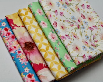 Könnte beinhalten: Ein Stapel aus fünf gefalteten Stoffquadraten mit verschiedenen Mustern. Das oberste Stück ist weiß mit einem zarten Blumenmuster, gefolgt von einem hellgrünen Stück mit rosa Blüten, einem gelben Stück mit geometrischem Muster, einem roten Stück mit großen Blumenmotiven und einem blauen Stück mit kleinen rosa Blüten.