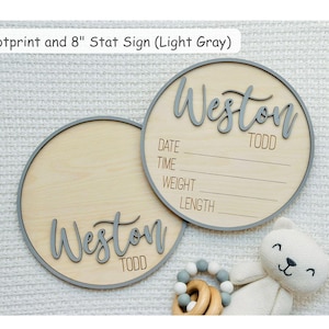 May include: Two light wood baby announcement signs with grey trim and lettering. One sign has the name "Weston Todd" and the other has the same name. The text "DATE, TIME, WEIGHT, LENGTH" is on one sign. The text "Footprint and 8" Stat Sign (Light Gray)" is at the top.