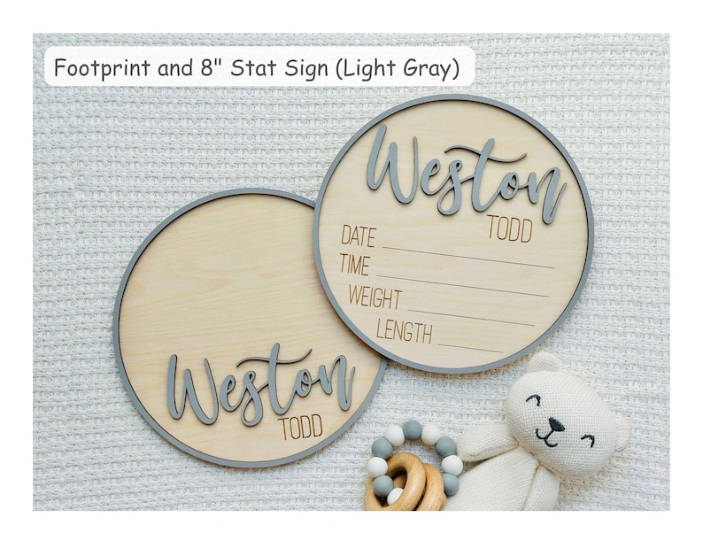 May include: Two light wood baby announcement signs with grey trim and lettering. One sign has the name "Weston Todd" and the other has the same name. The text "DATE, TIME, WEIGHT, LENGTH" is on one sign. The text "Footprint and 8" Stat Sign (Light Gray)" is at the top.