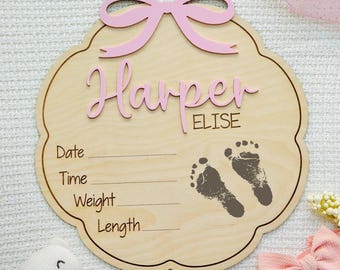 Letrero de madera personalizado para anunciar el nacimiento de una niña con forma de lazo, con nombre de bebé, huella y estadísticas.