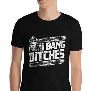 Puede incluir: Una camiseta negra con un gráfico blanco de una persona conduciendo un ATV con el texto "I Bang Ditches" en una fuente blanca desgastada.