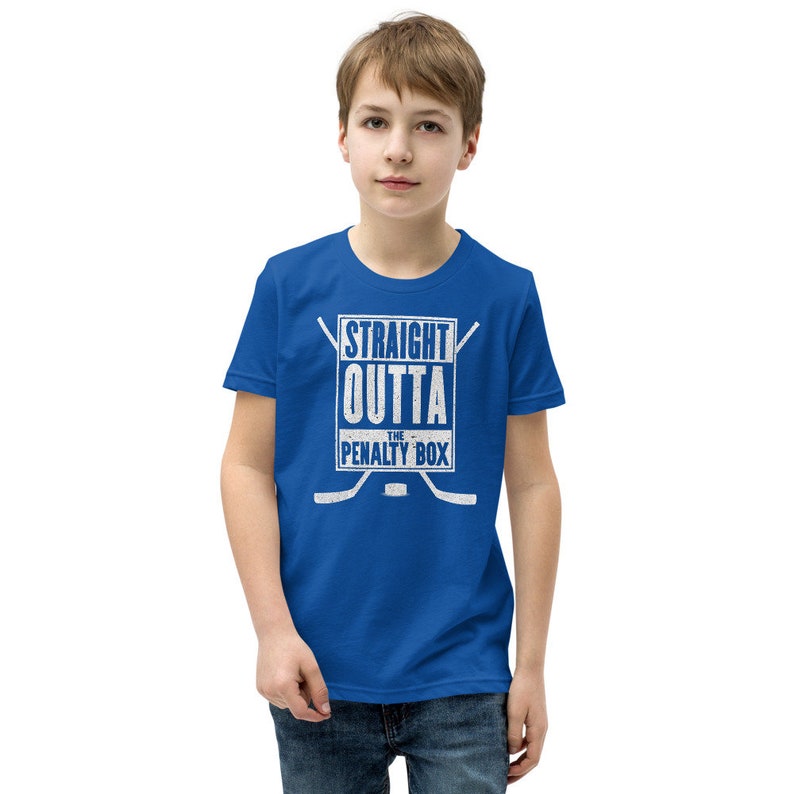 May include: A royal blue youth t-shirt with a white graphic that says "Straight Outta The Penalty Box" with hockey sticks on either side of the text.