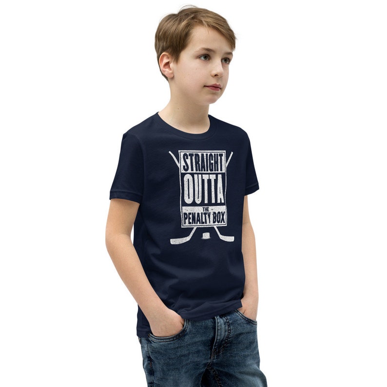 May include: A navy blue youth t-shirt with a white graphic that says "Straight Outta The Penalty Box" with two hockey sticks crossed behind the text.