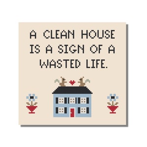 Könnte beinhalten: Kreuzstichmuster mit einem blauen Haus mit roten Verzierungen und zwei Eichhörnchen auf dem Dach. Der Text "A clean house is a sign of a wasted life." befindet sich über dem Haus.