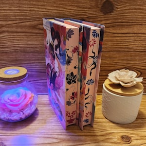 May include: Two hardcover books with colorful floral and abstract designs. The books are stacked on top of each other. The book on the bottom has the title "In the Bloom" on the cover.