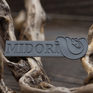 May include: A grey plastic bookmark with the word "MIDORI" embossed on it. The bookmark features a stylised snake design.