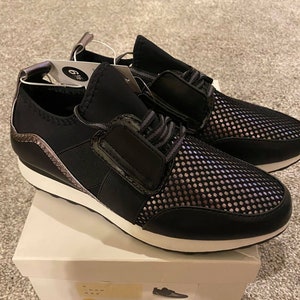 以下が含まれることがあります： 白のソールとメッシュのアッパーが付いた黒いスニーカーのペア。スニーカーは側面に銀色のアクセントがあり、箱には「a new day 6 1/2」と書かれた黒と白のラベルが付いています。