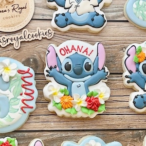 Pode incluir: Um conjunto de seis biscoitos de açúcar decorados com o personagem Stitch do filme da Disney Lilo & Stitch. Os biscoitos são decorados com glacê azul, rosa, branco, verde e vermelho. Os biscoitos são decorados com as palavras "Ohana!" e "Mina".