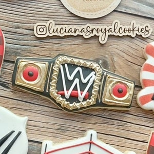 May include: A gold and black wrestling championship belt with a red and white "W" logo. The belt is decorated with gold studs and a red and black strap.