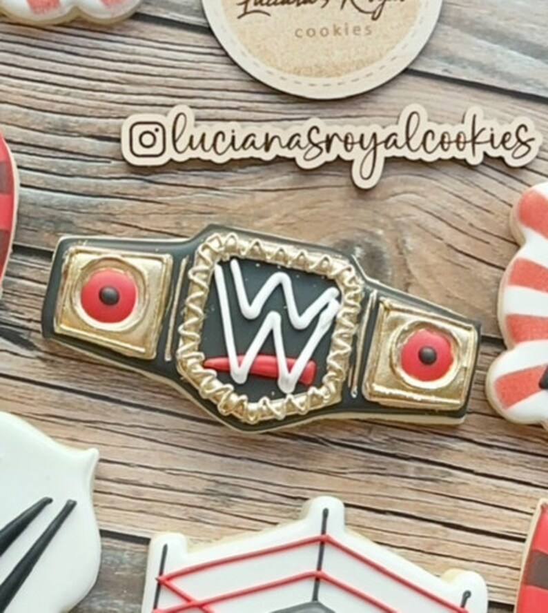 May include: A gold and black wrestling championship belt with a red and white "W" logo. The belt is decorated with gold studs and a red and black strap.