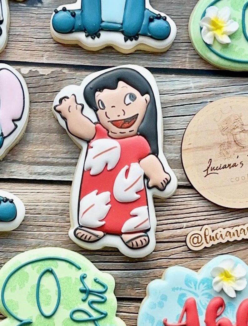 May include: A set of decorated sugar cookies featuring characters from the Disney movie Lilo & Stitch. The cookies are decorated with colourful icing and feature Lilo, Stitch, and a flower.