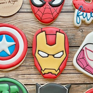 May include: A collection of superhero-themed cookies, including Spider-Man, Iron Man, Captain America, Hulk, Black Panther, and a red and white cookie with the word "five" on it.