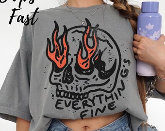 May include: A grey t-shirt with a skull graphic and the text "Everything's Fine" in black lettering. The skull has flames for eyes and a black and white design.