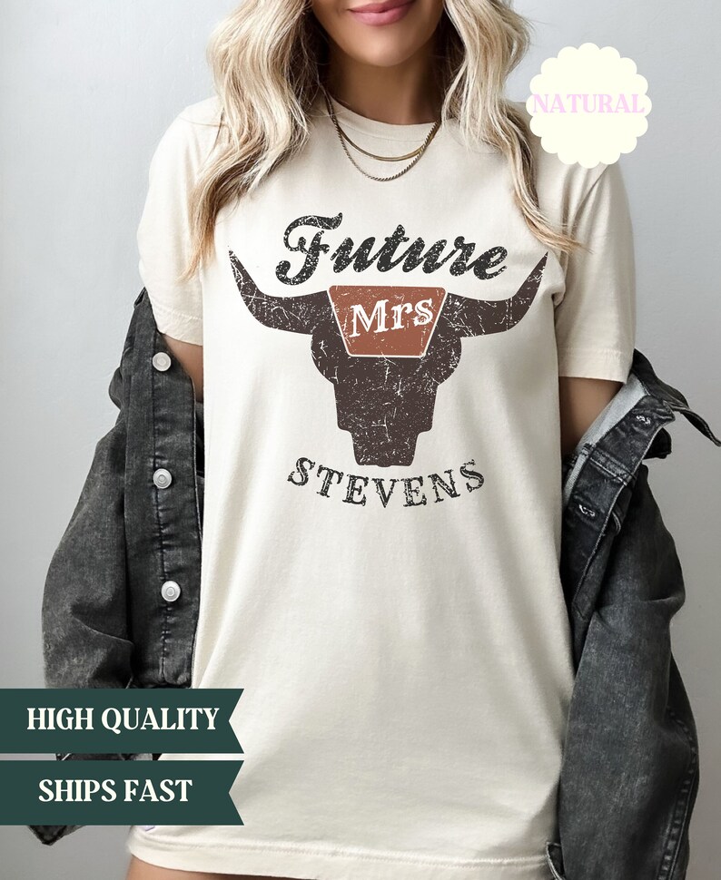 May include: A beige t-shirt with a distressed brown bull skull graphic. The text "Future Mrs. Stevens" is printed on the shirt.