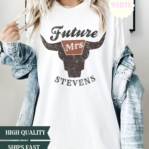 May include: White t-shirt with a distressed brown bull skull graphic. The text "Future Mrs. Stevens" is printed on the shirt.