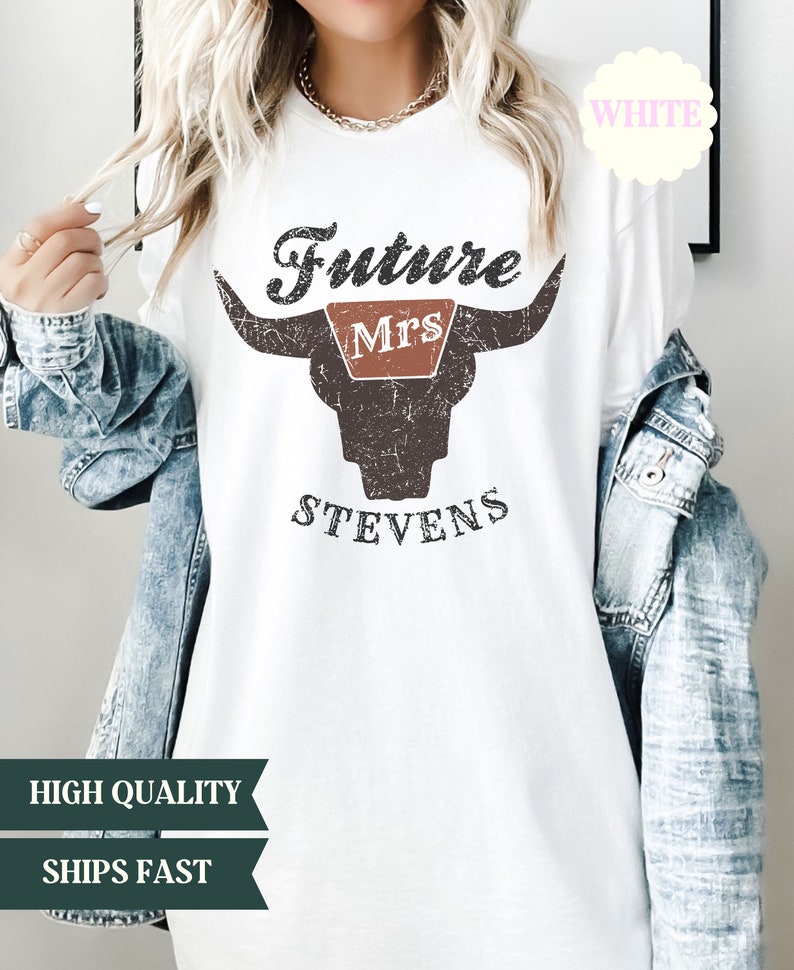 May include: White t-shirt with a distressed brown bull skull graphic. The text "Future Mrs. Stevens" is printed on the shirt.