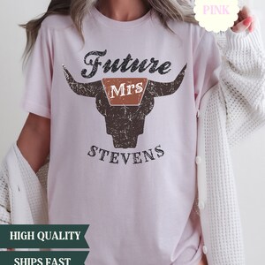 May include: Pink t-shirt with a distressed graphic of a bull's head with the text "Future Mrs. Stevens" on it.